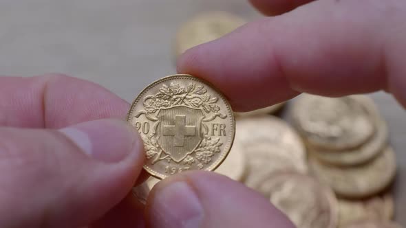 Person holding polished golden twenty franc coin from year 1947,close up. Bunch of coins in backgrou