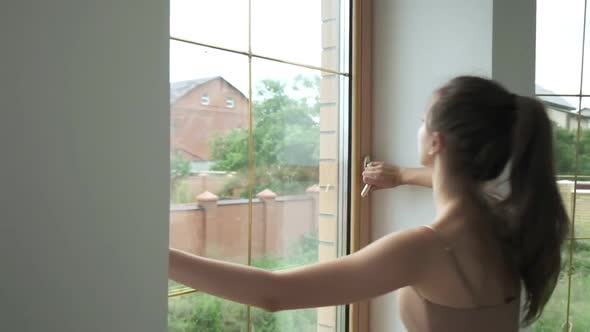 Young Sporty Brunette Pretty Female with Ponytail Opens Window Closeup