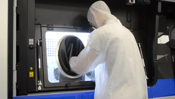 A Man in a White Protective Suit Stands Near a Large 3D Printer