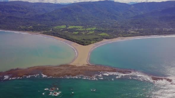 Aerial shot pulling away from the whale tail shaped rocky point of Punta Uvita surrounded by bright