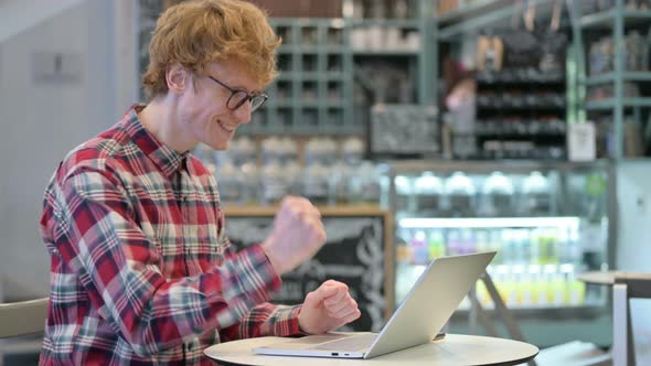 Excited Young Redhead Man Celebrating Success on Laptop 
