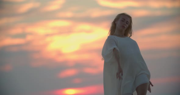 Blonde Lady in White Dress is Dancing During Sunset Colorful Sky in Background