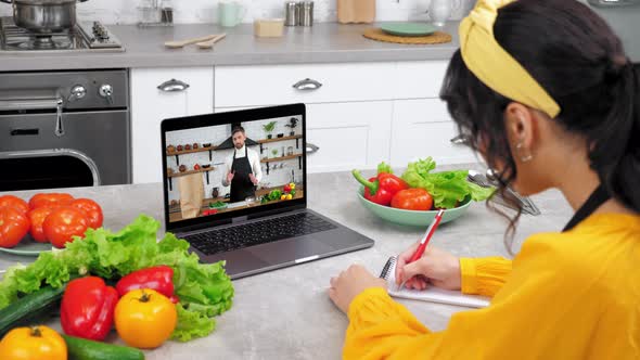 Woman in Kitchen Study Online Video Call Laptop Greets Chef Writes in Notebook