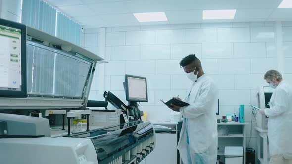 A Diverse Team Works in the Lab Using Tablet Computers Wearing Masks and Gowns