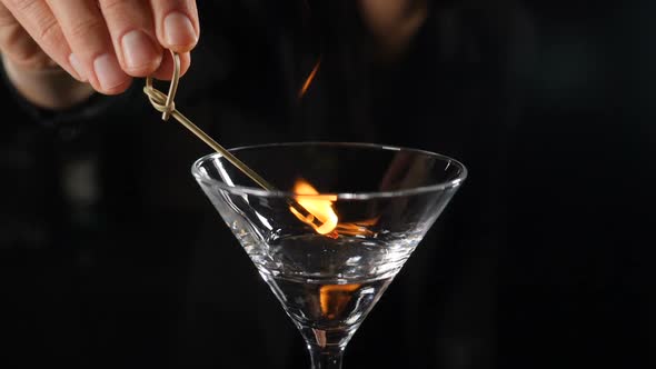 Female Bartender Setting Fire with Burning Stick on Alcohol Cocktail in Slow Motion. Fire Ignition