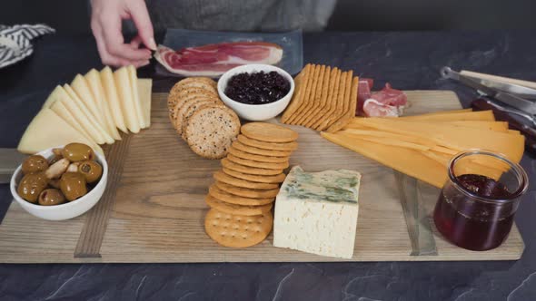 Arranging gourmet cheese, crakers, and fruits on a board for a large cheese board.