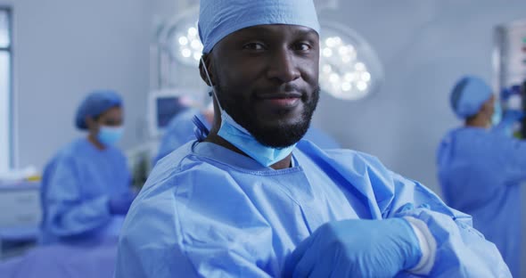 Portrait of african american male surgeon standing in operating theatre smiling to camera