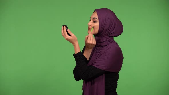 A Young Beautiful Muslim Woman Puts on Makeup and Looks Into a Mirror  Green Screen Background