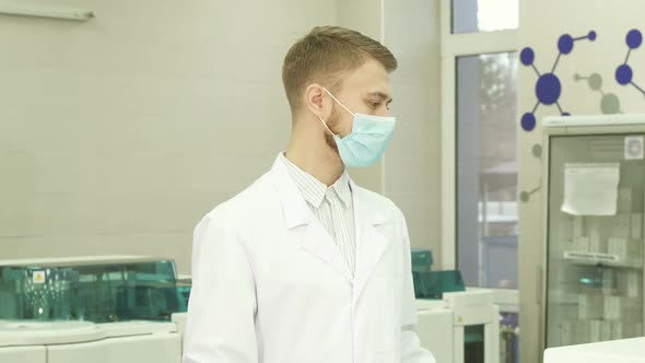 A Serious Lab Assistant Stands in the Middle of the Laboratory and Turns His Head Into the Camera