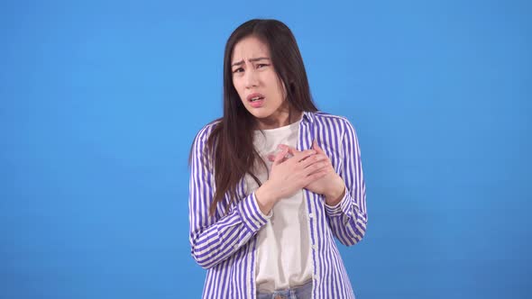 Young Asian Woman with a Heartache Stands on a Blue Background