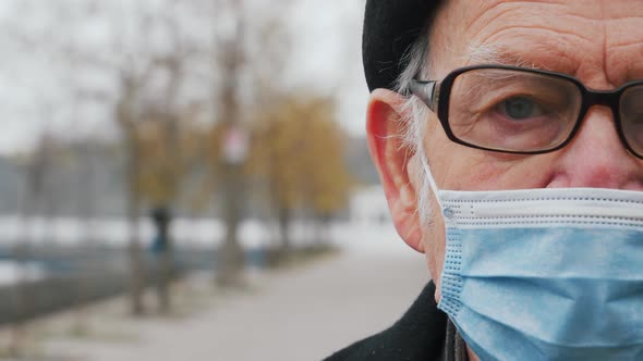 Close up of half face of upset Caucasian elderly senior in medical mask looking straight to camera w