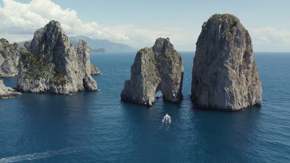 Boats cruise through natural arch of Faraglioni (sea stacks) in Capri; aerial