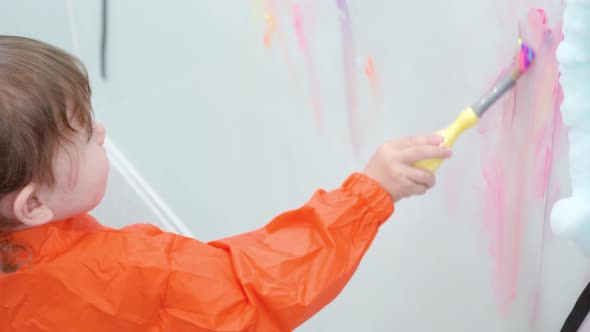 Adorable 2-year-old Girl Painting On Playroom Wall In A Toddler Cafeteria. high angle, slow motion