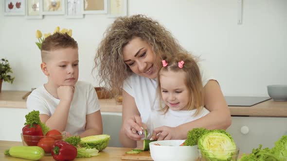 The Children Together with Their Mother Prepare a Salad at the Table in the Kitchen