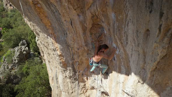 Young Powerful Athletic Man Rock Climber with Long Hair Climbing on Overhanging Cliff