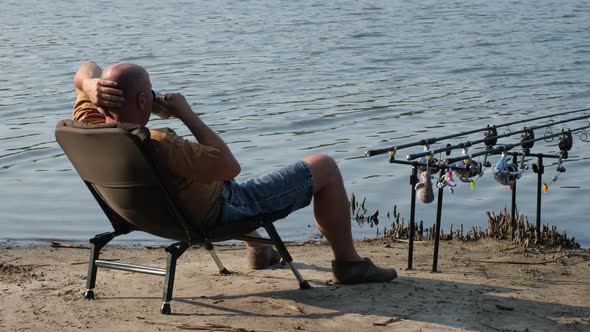 Fisherman with Hot Drink in Mug Waiting a Bite with Carp Fishing Equipment