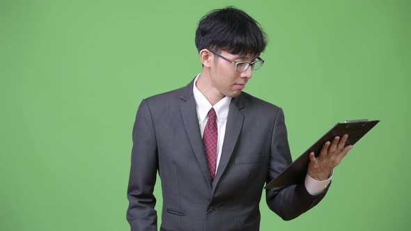 Young Asian Businessman Reading and Thinking with Clipboard