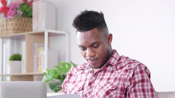 Busy African man working from home holding a lot of financial document, using laptop