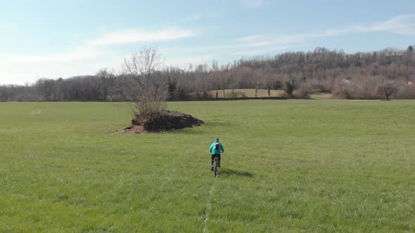 Aerial: man having fun by riding mountain bike in the grass on sunny day, scenic alpine landscape