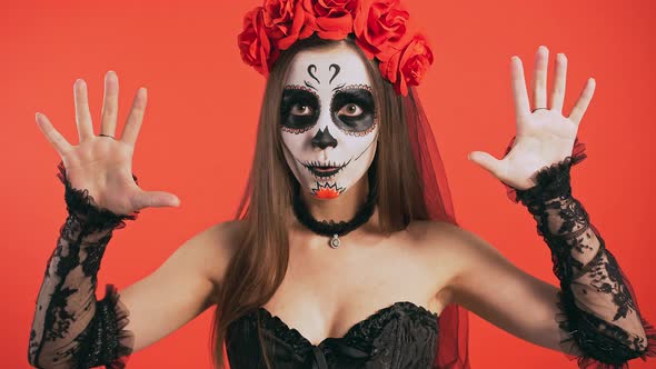 Day of Dead Woman with Sugar Skull Makeup Scaring you By Hands Saying Boo and Smiling Posing on Red