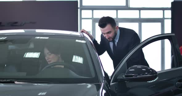 Positive Handsome Male Dealer Consulting Successful Businesswoman Sitting on Driver's Seat