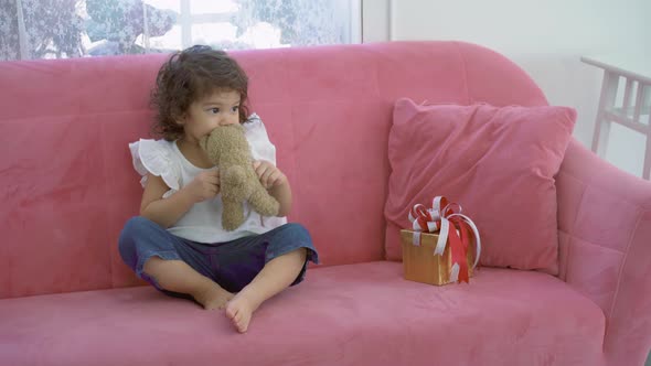 Cute little girl sitting on the sofa playing bear doll and feeling happy at home	