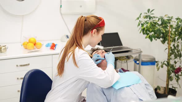 Female Dentist Treating Tooth of Young Male Patient Lying in Dental Chair Filling Root Canal