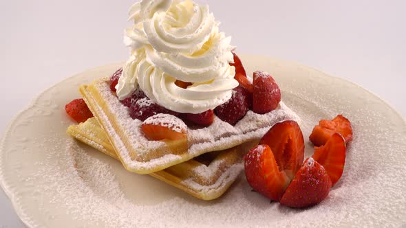 Belgian waffles with strawberry, whipped cream and powdered sugar on a plate on a white background.