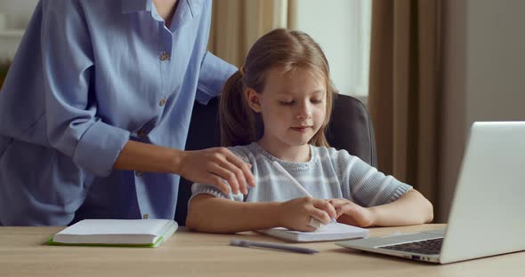 Mother Controls Little Cute Daughter, Checks Homework, Child Sits at Table Writes on Paper, Learns