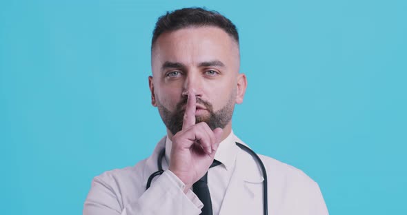 Portrait of Serious Doctor Holding Finger on Lips, Blue Studio Background