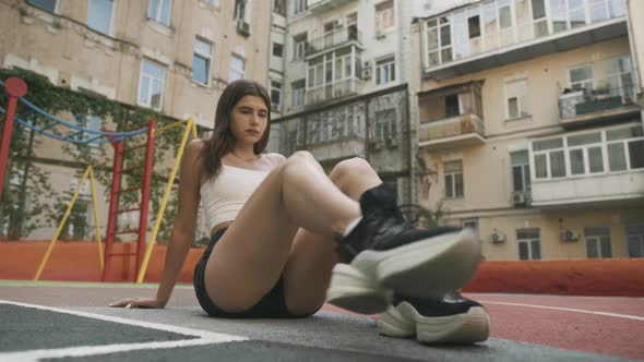 Fit Slender Woman Sitting on Outdoor Court Looking at Camera