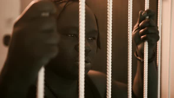 Depresed African American Black Man Holding Bars in the Prison and Shaking Head