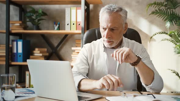 Middleaged Male Looking at Laptop Taking Off Glasses and Massaging Temples Having Headache Sitting