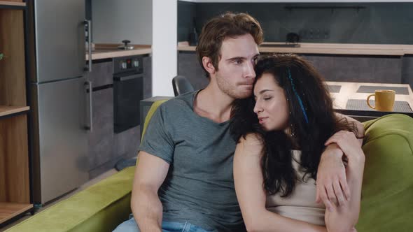 Happy Young Couple Are Tenderly Embracing and Sitting on the Sofa at Home. The Husband Hugs His Wife