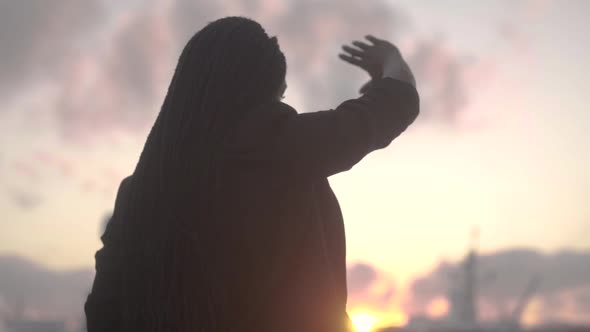 Serene black woman outstretching arm against bright setting sun