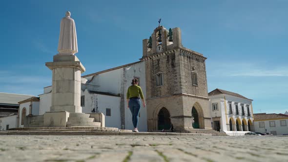 Girl Tourist Walks Through the Square of the Ancient Church of Santa Maria Near the Monument Bishop