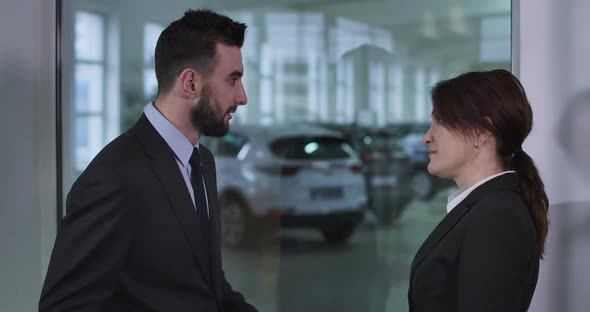 Side View of Serious Caucasian Man and Woman Standing in Car Dealership and Talking