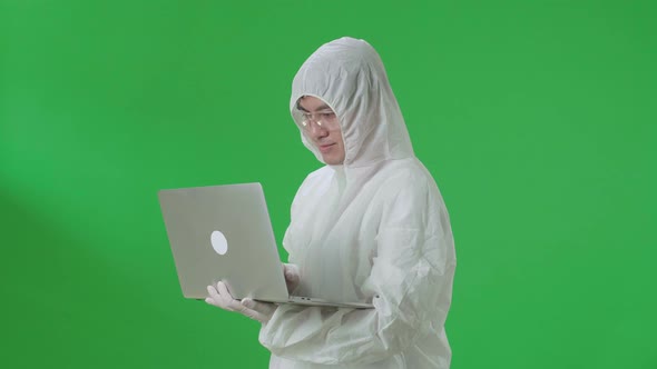 Side View Of Asian Man Wear Uniform Ppe Holding And Working With Laptop In The Green Screen Studio