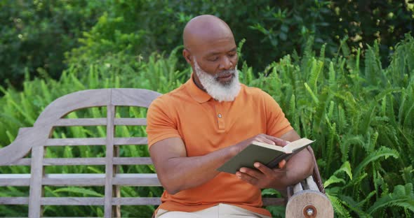 African american senior man reading a book while sitting on a bench in the garden