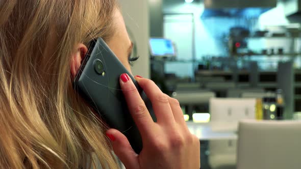 A Woman Sits at a Table in a Restaurant and Talks on a Smartphone - Closeup