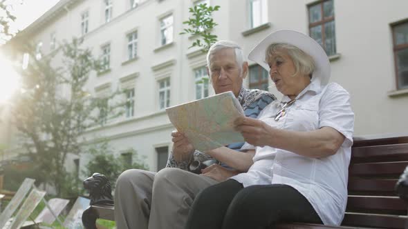 Senior Tourists Sitting on Bench with a Map in Hands Looking for Route