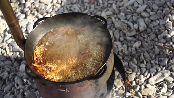 Uzbek Pilaf in a Cauldron Boils and Exudes Steam on a Stove