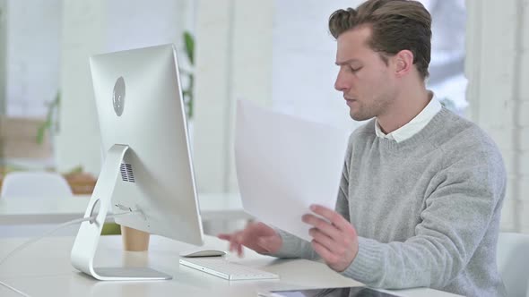 Serious Young Man Doing Paperwork in Office 