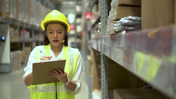 Asian woman warehouse worker doing stocktaking of products management in cardboard box on shelves