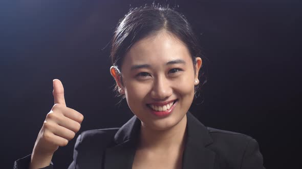 Smiling Asian Speaker Woman In Business Suit Showing Thumbs Up Gesture While Standing On Stage