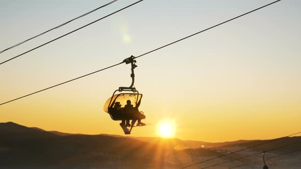Skier Silhouettes Move on Chairlift Against Setting Sun Disk