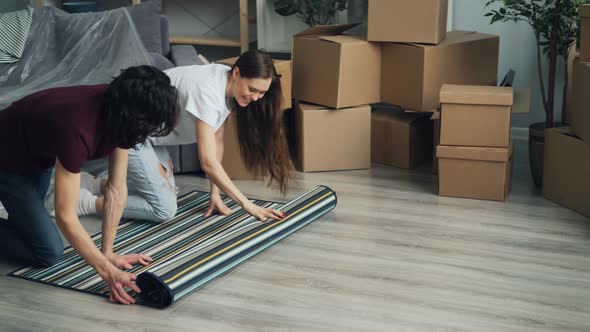 Man and Woman Rolling Out Carpet on Floor After Moving To New Apartment Together