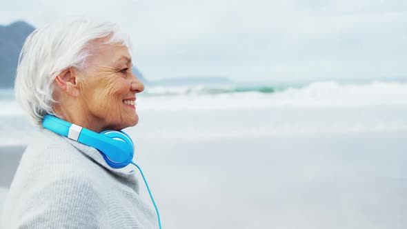 Senior woman wearing headphone around neck while walking on beach