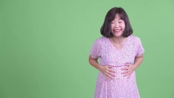 Happy Asian Pregnant Woman Showing To the Back and Looking Surprised