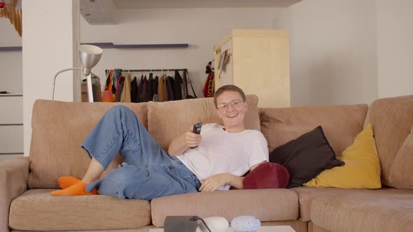 Young Caucasian Happy Woman in a White Tshirt and Blue Jeans Crash on the Sofa to See Tv